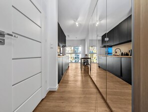 A modern kitchen with dark cabinetry, a wooden floor, and a view of trees through large windows. - Magnolia Bloom Studio (Wrocław)