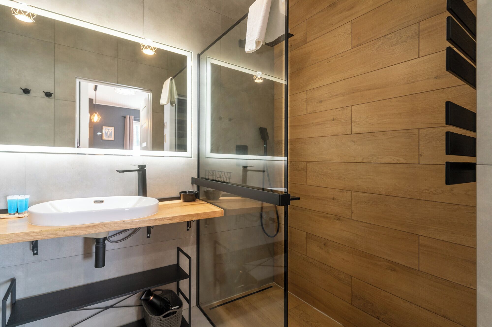 A modern bathroom with a wooden floor, a white sink, and a glass shower enclosure.
