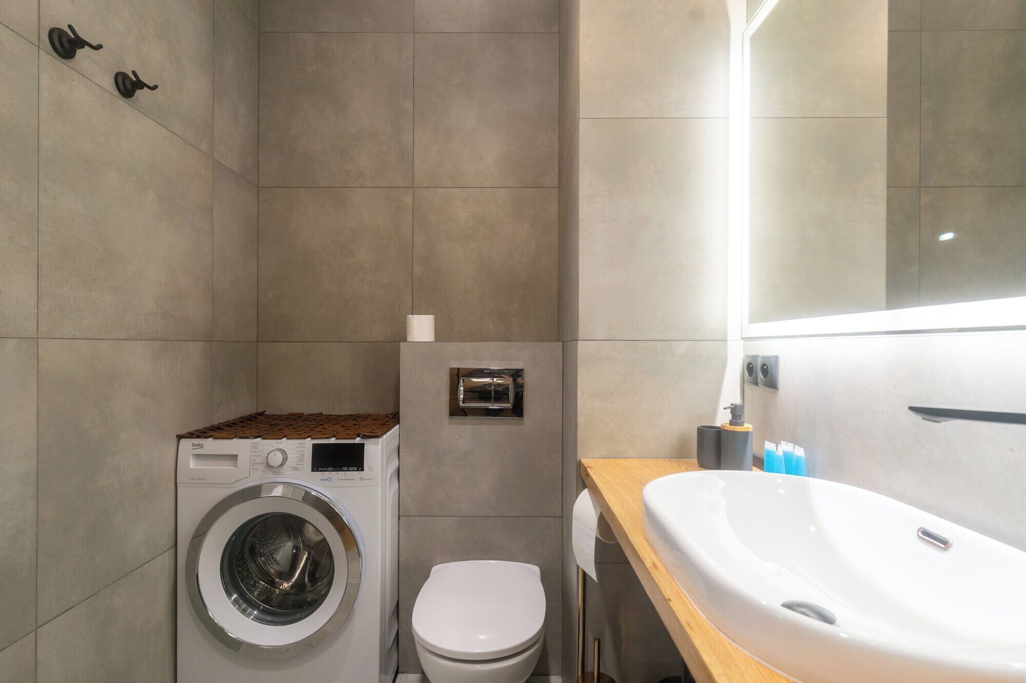 Een kleine badkamer met een wasmachine, toilet en een wastafel met spiegel.