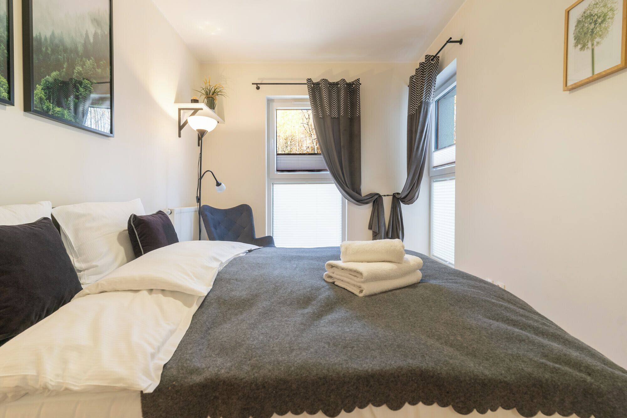 A neatly made bed with a grey blanket, a bedside lamp, and a window with curtains.