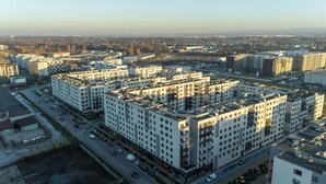 Un immeuble d’habitation de grande hauteur, avec de nombreux étages, un espace de stationnement à l’avant et une vue sur le paysage urbain environnant.