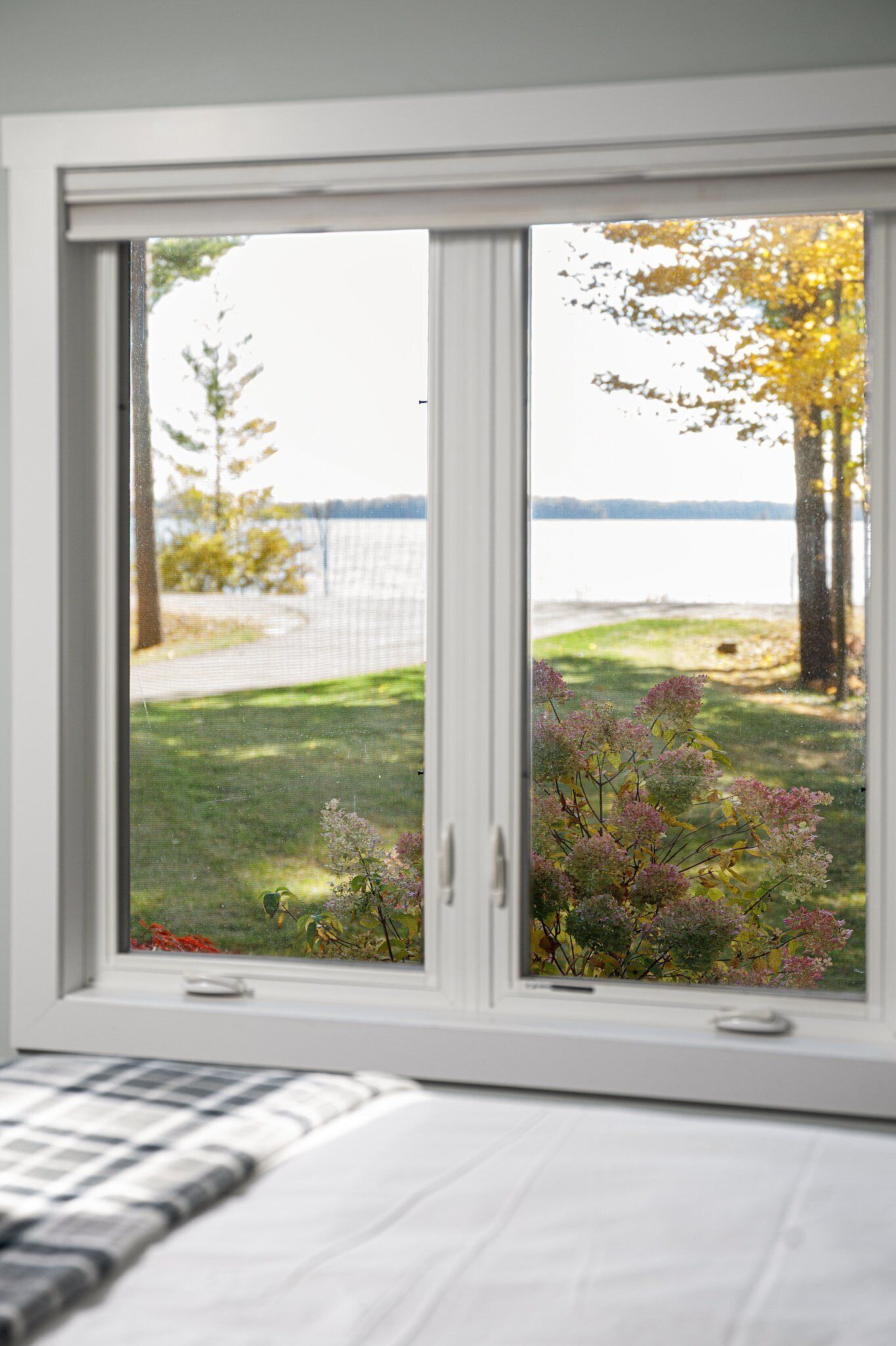 A bedroom with a window overlooking a grassy area and a body of water.