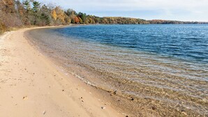 A beach with clear water, sandy shore, and trees with autumn foliage. - The Long Lake Escape (Traverse City)