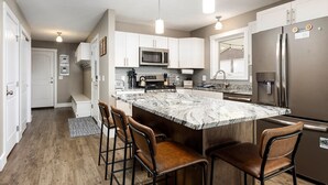 A modern kitchen with a marble island, stainless steel appliances, and bar stools. - The Long Lake Escape (Traverse City)