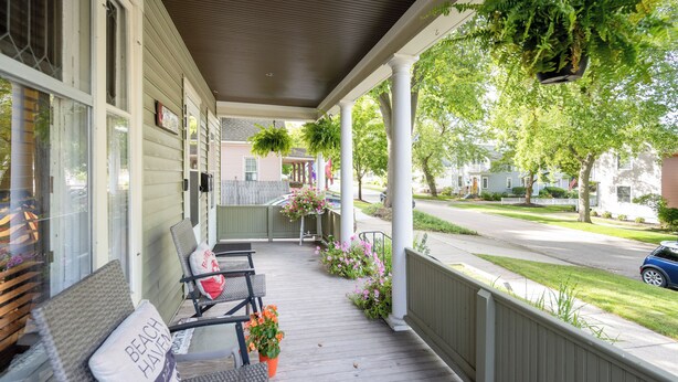 A covered porch with outdoor seating, hanging plants, and a view of the street. - Updated Home near downtown Grand Haven - First Floor (Grand Haven)