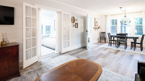 Una habitación amplia con una gran mesa de madera para comer, un televisor en la pared y una cama con vistas al exterior.