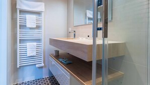 A modern bathroom with a wooden vanity, a glass shower enclosure, and a towel rack with multiple towels. - Caracalla Room with private patio (Bordeaux)