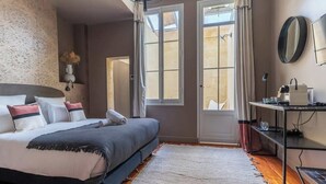 A bedroom with a bed, a bedside table, a mirror, and a window. - Caracalla Room with private patio (Bordeaux)
