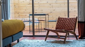 A room with a bed, a woven chair, a table, and chairs against a wooden wall. - Large Magna room with private terrace (Bordeaux)