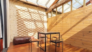A room with a wooden floor, a table with chairs, a leather bench, and a lattice wall. - Large Magna room with private terrace (Bordeaux)