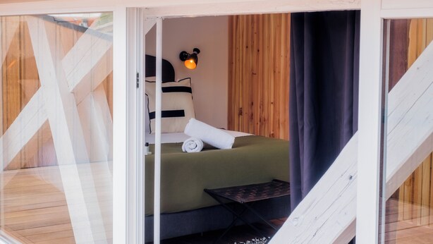 A cozy bedroom with a bed, pillows, a nightstand, and a wall-mounted lamp. - Lixus Suite with private terrace and kitchen (Bordeaux)