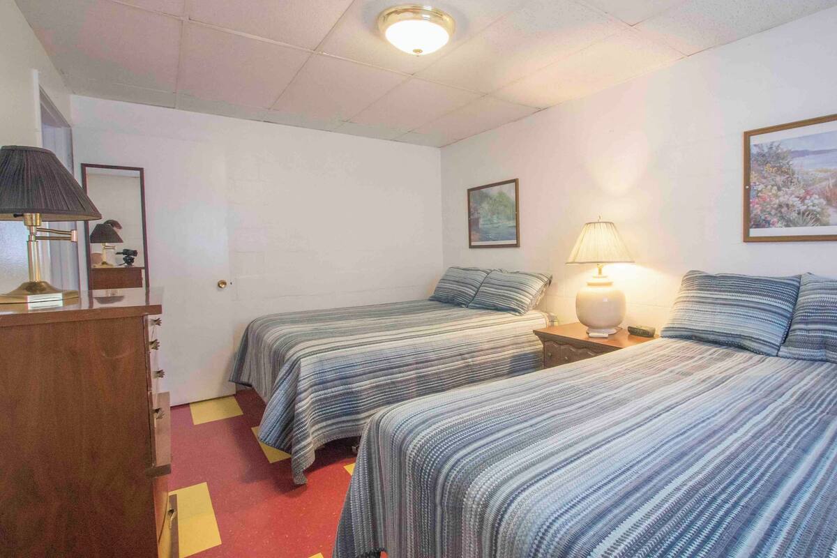 A bedroom with two beds, a nightstand, a lamp, a framed picture, and a wooden dresser.