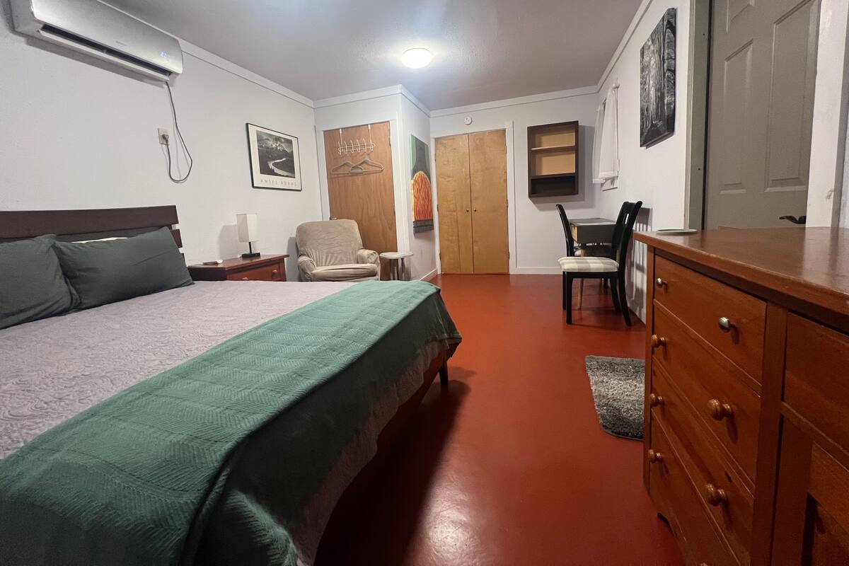 A hotel room with a bed, a chair, a desk, a dresser, and a wardrobe.