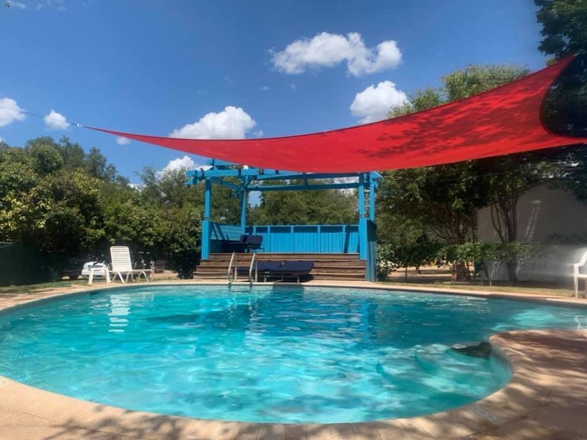 A swimming pool with a blue deck, a red canopy, and a white lounge chair.