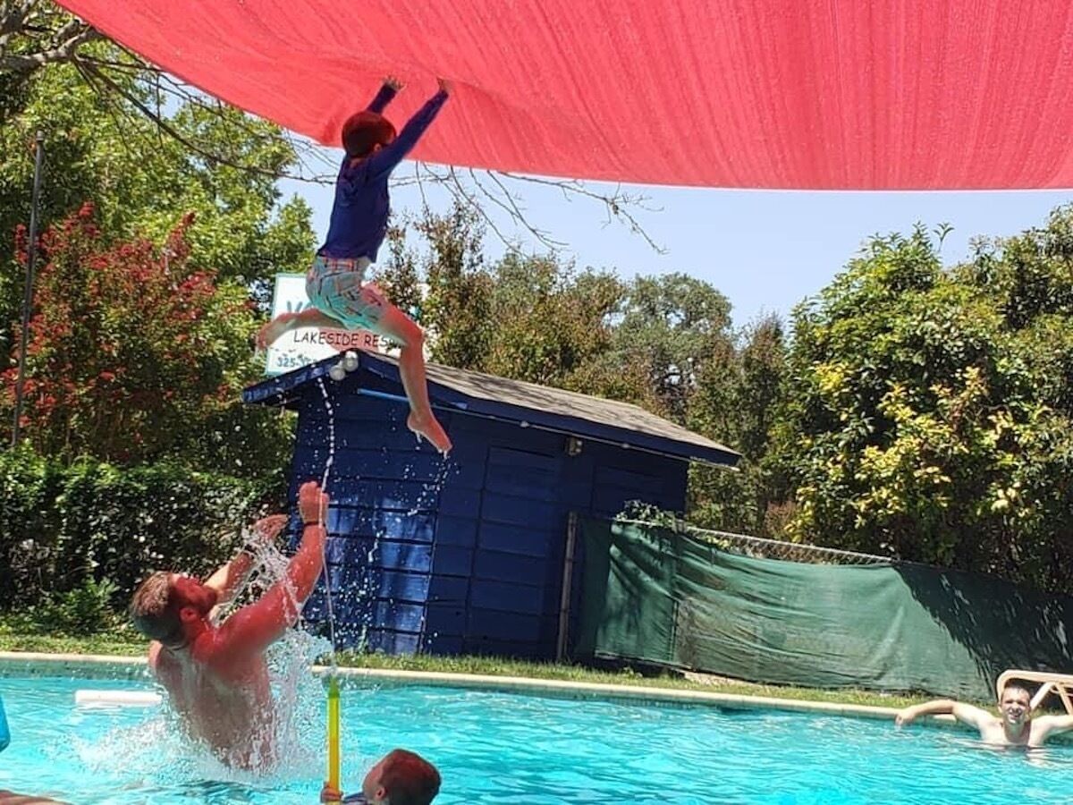 A person jumping into a pool from a structure with a red canopy.