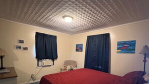 A bedroom with a red bedspread, a ceiling with a geometric pattern, and a painting of fish on the wall. - Lakeside Valentine (Kingsland)