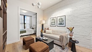 A modern living room with a white brick wall, a sofa, a coffee table, and a side table with a vase. - The Brick Hotel (Toronto)
