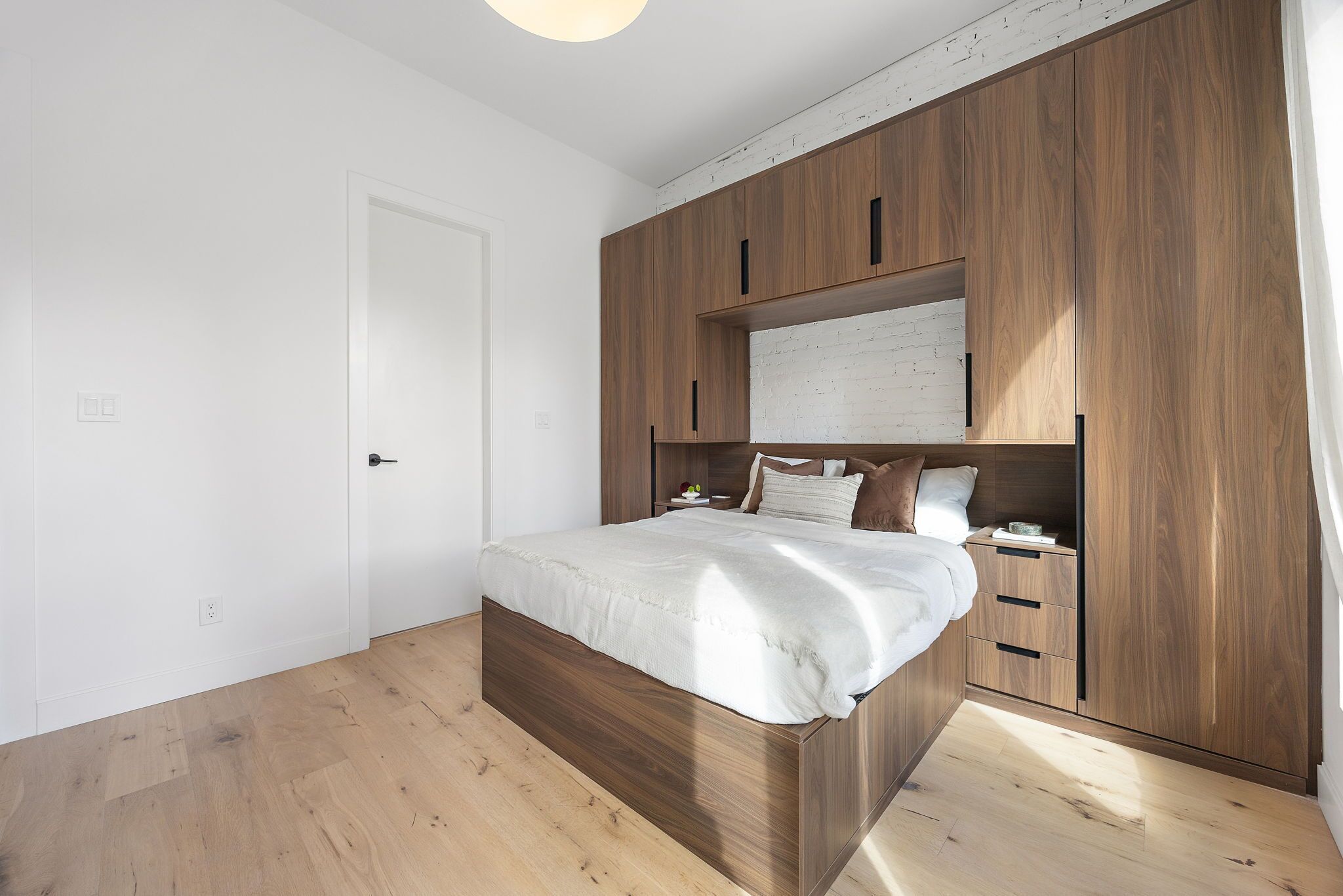 A bedroom with a wooden bed frame, white bedding, and built-in wooden wardrobe with multiple compartments.