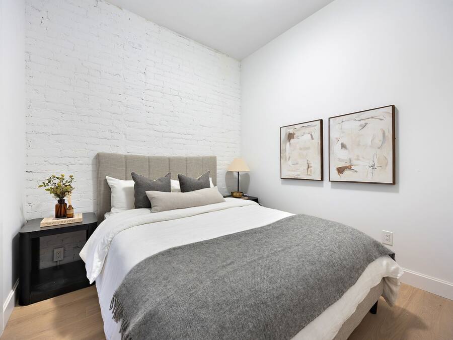 Un dormitorio moderno con una pared de ladrillo blanco, una colcha gris y dos cuadros abstractos en la pared.