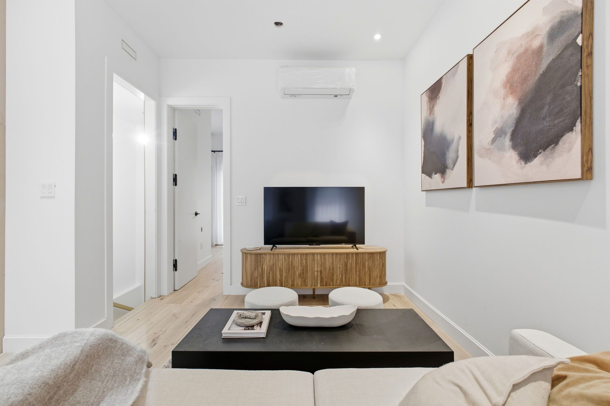 A modern living room with a flat-screen TV on a wooden console, a black coffee table, and a beige sofa.