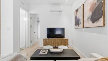 A modern living room with a flat-screen TV on a wooden console, a black coffee table, and a beige sofa.