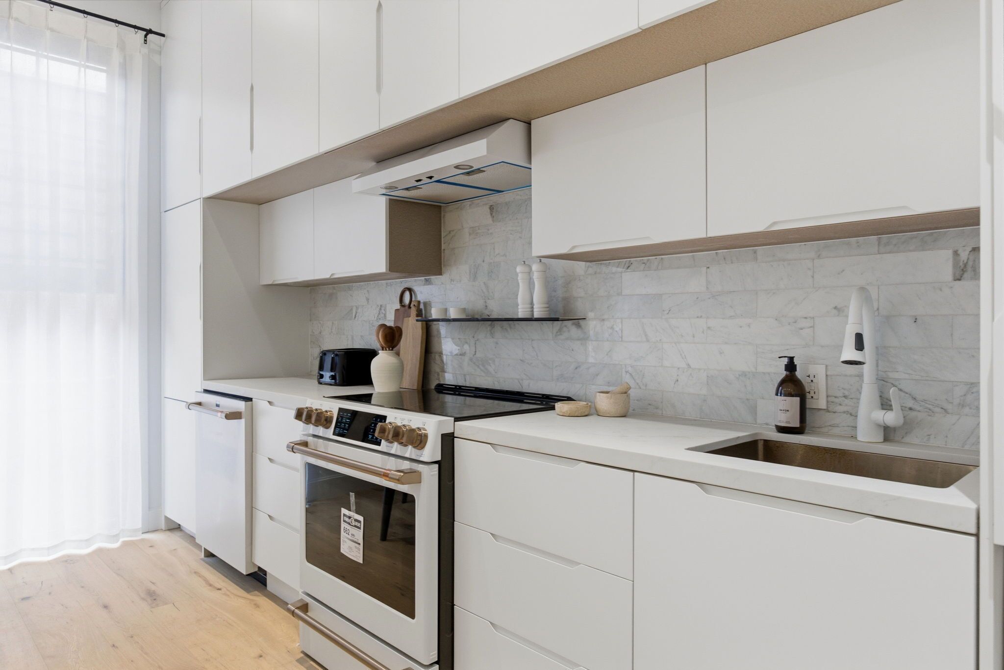 Una cocina moderna con armarios blancos, horno integrado, pileta de acero inoxidable y salpicadero de mármol.