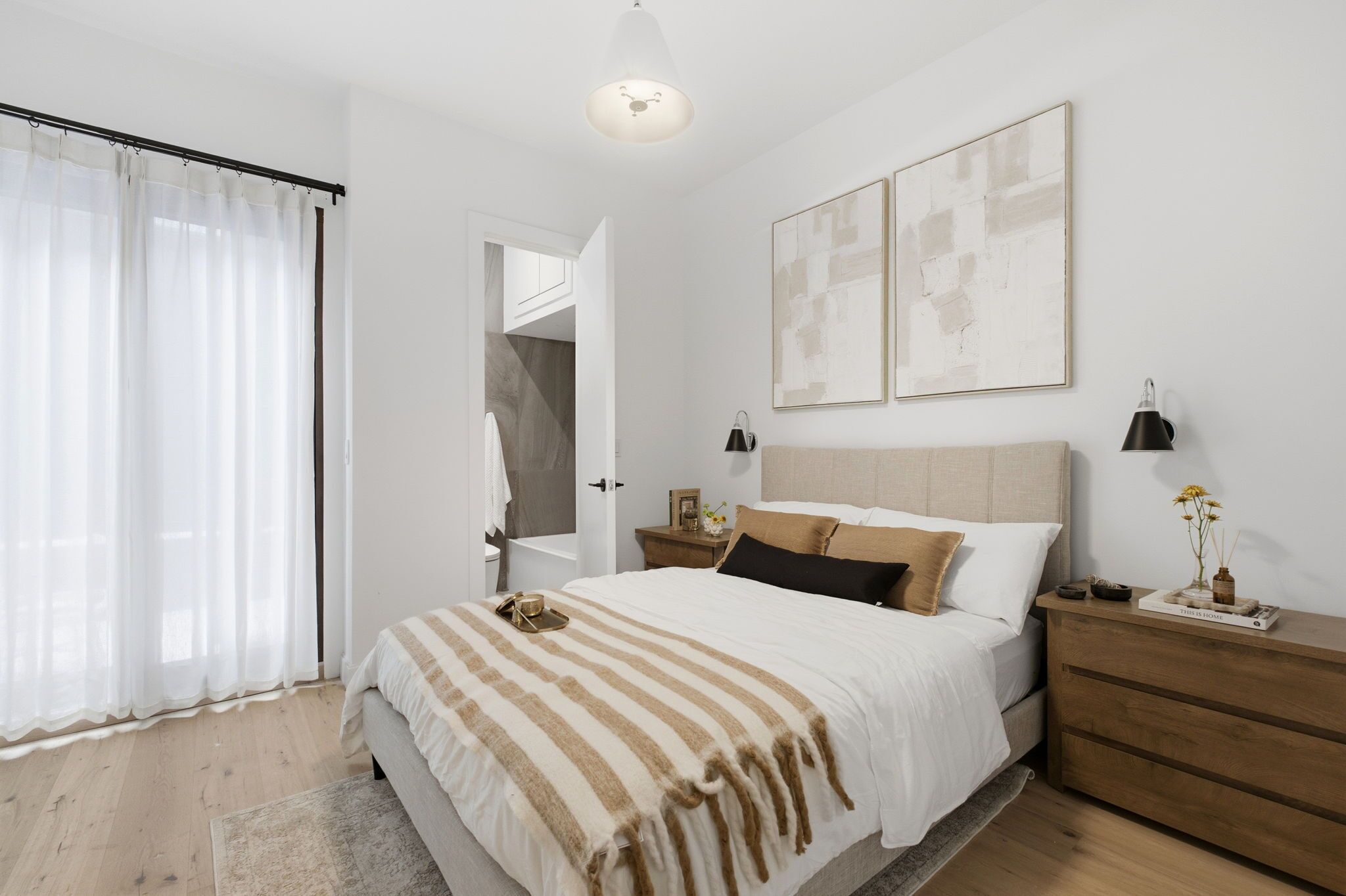 Un dormitorio con una cama grande, una mesita de noche de madera, una mesita con lámpara y vistas al baño.