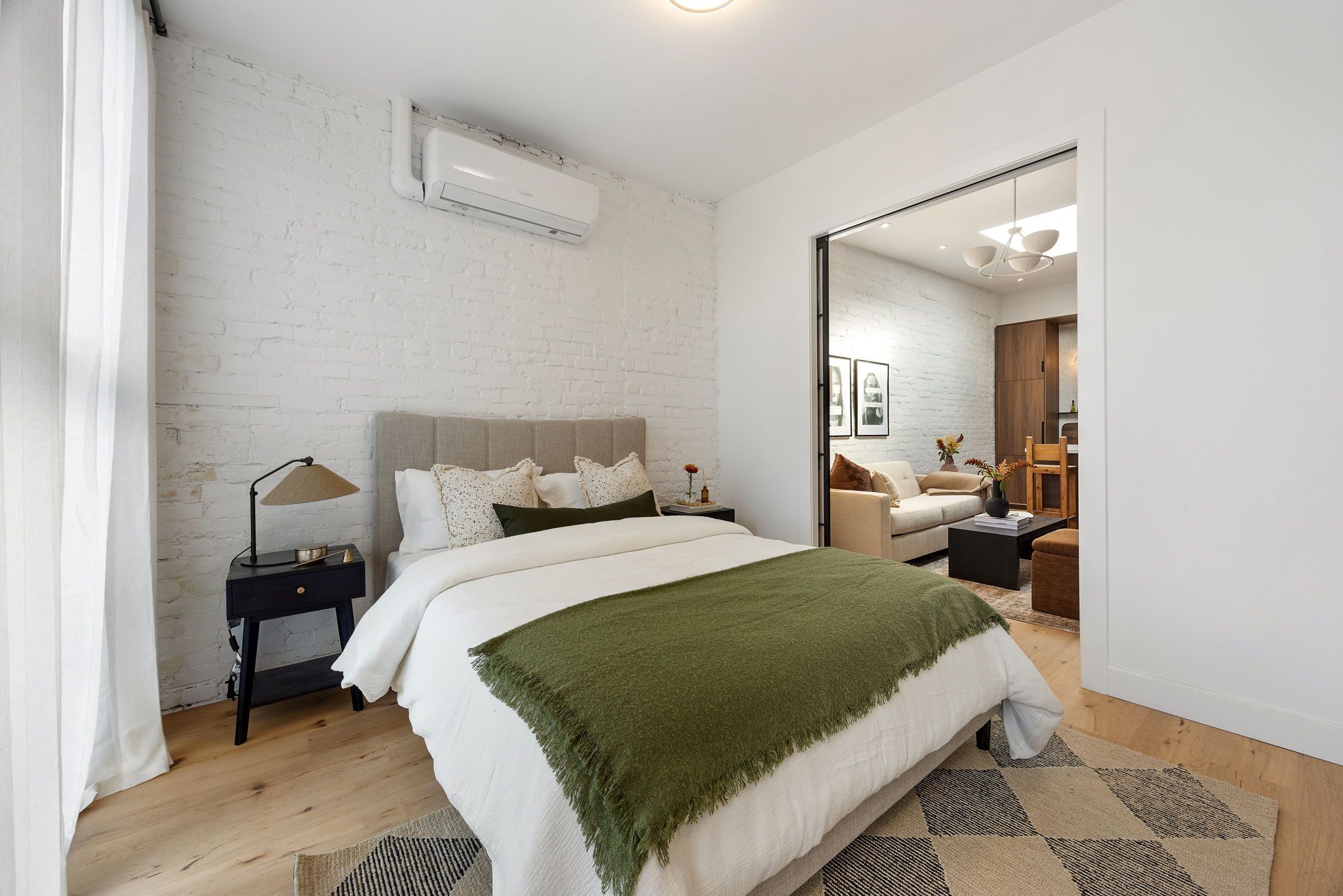 A modern bedroom with a large bed, a bedside table, a mirror, and a wooden floor.