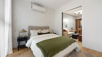A modern bedroom with a large bed, a bedside table, a mirror, and a wooden floor.