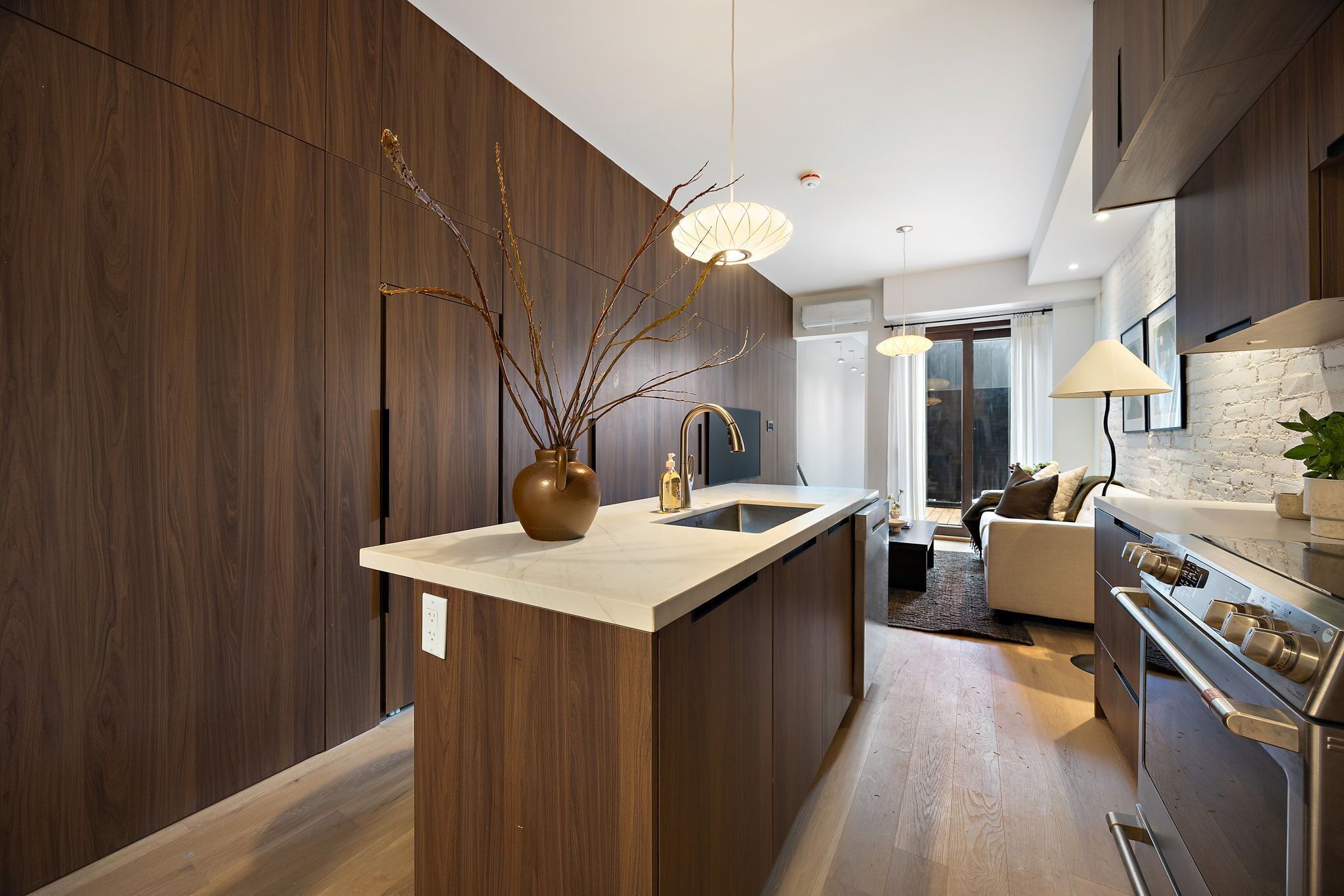 Una cocina moderna con armarios de madera oscura, una isla central, electrodomésticos de acero inoxidable e iluminación colgante.