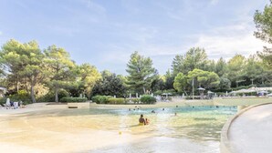 Una piscina pública con agua cristalina, rodeada de árboles y zonas de sombra.