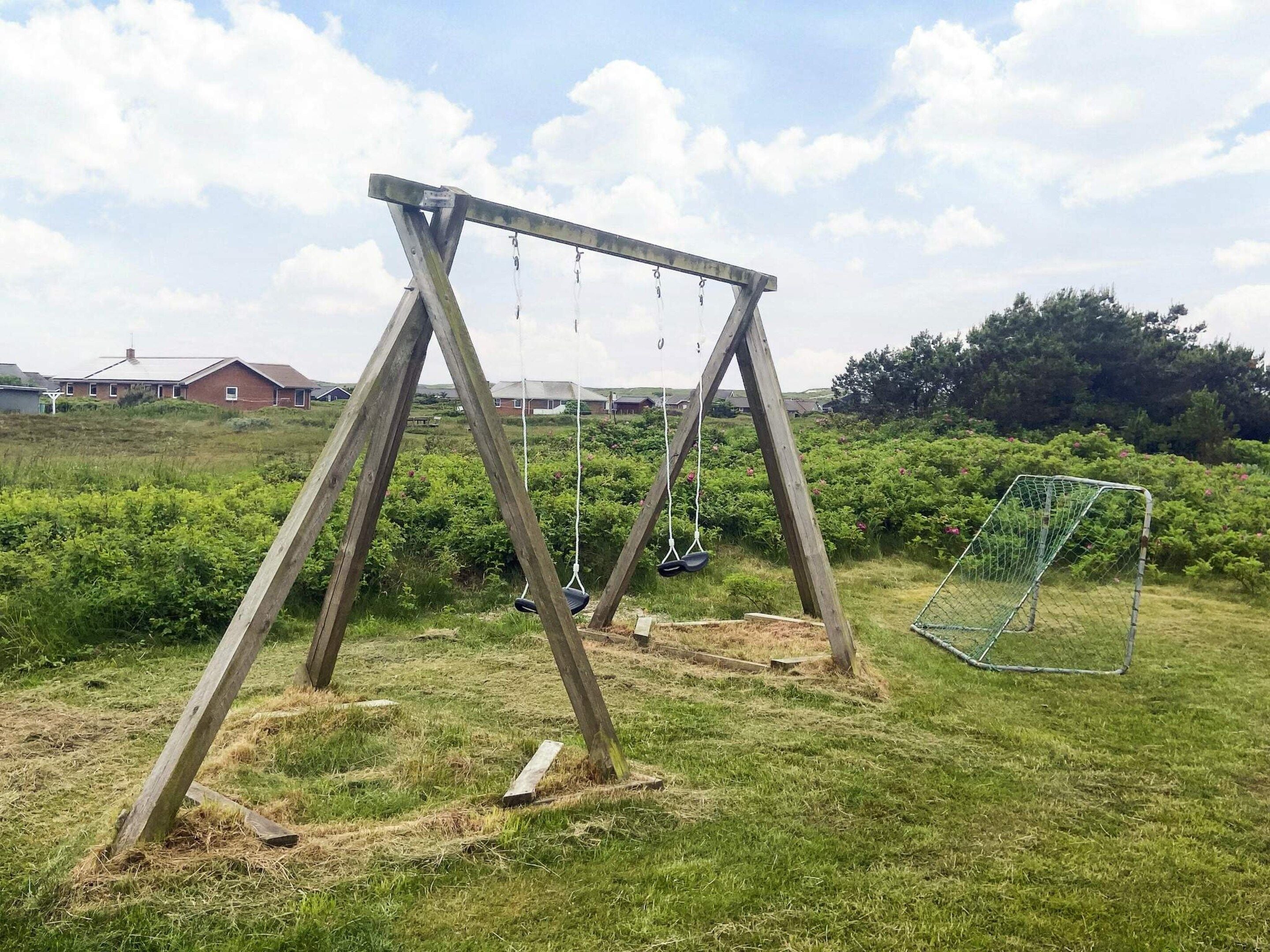 Un columpio de madera en un campo cubierto de césped, con un arco de fútbol de fondo.