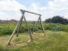Un columpio de madera en un campo cubierto de césped, con un arco de fútbol de fondo.
