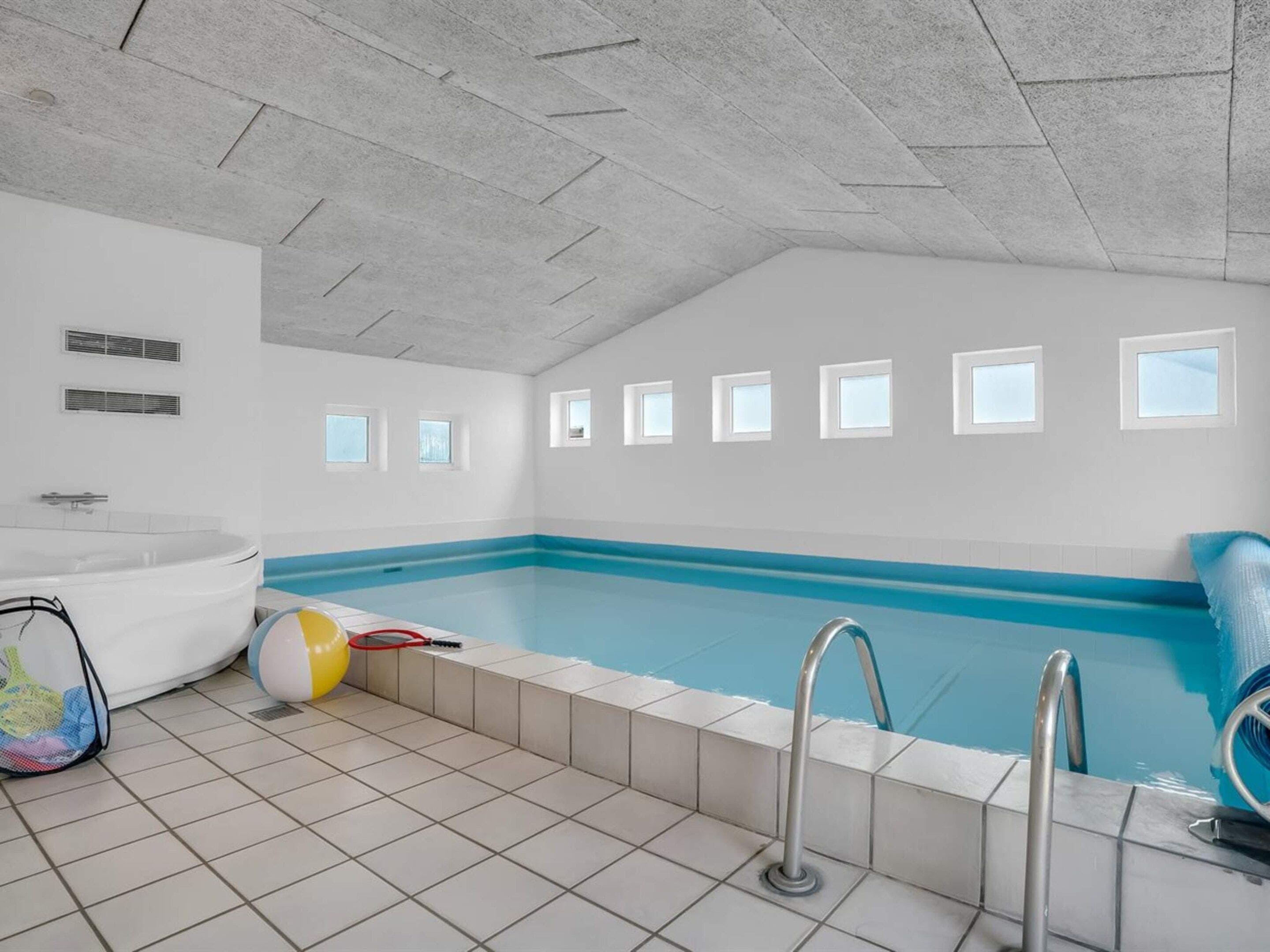 Una piscina con piso de baldosas, una bañera blanca y un ventanal con vistas.