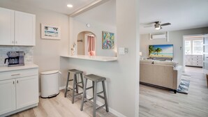 A modern kitchen with white cabinets, a coffee maker, and a small island with stools. - Across from the beach - Bella by the Sea by SeaBreeze Vacation (Bradenton Beach)