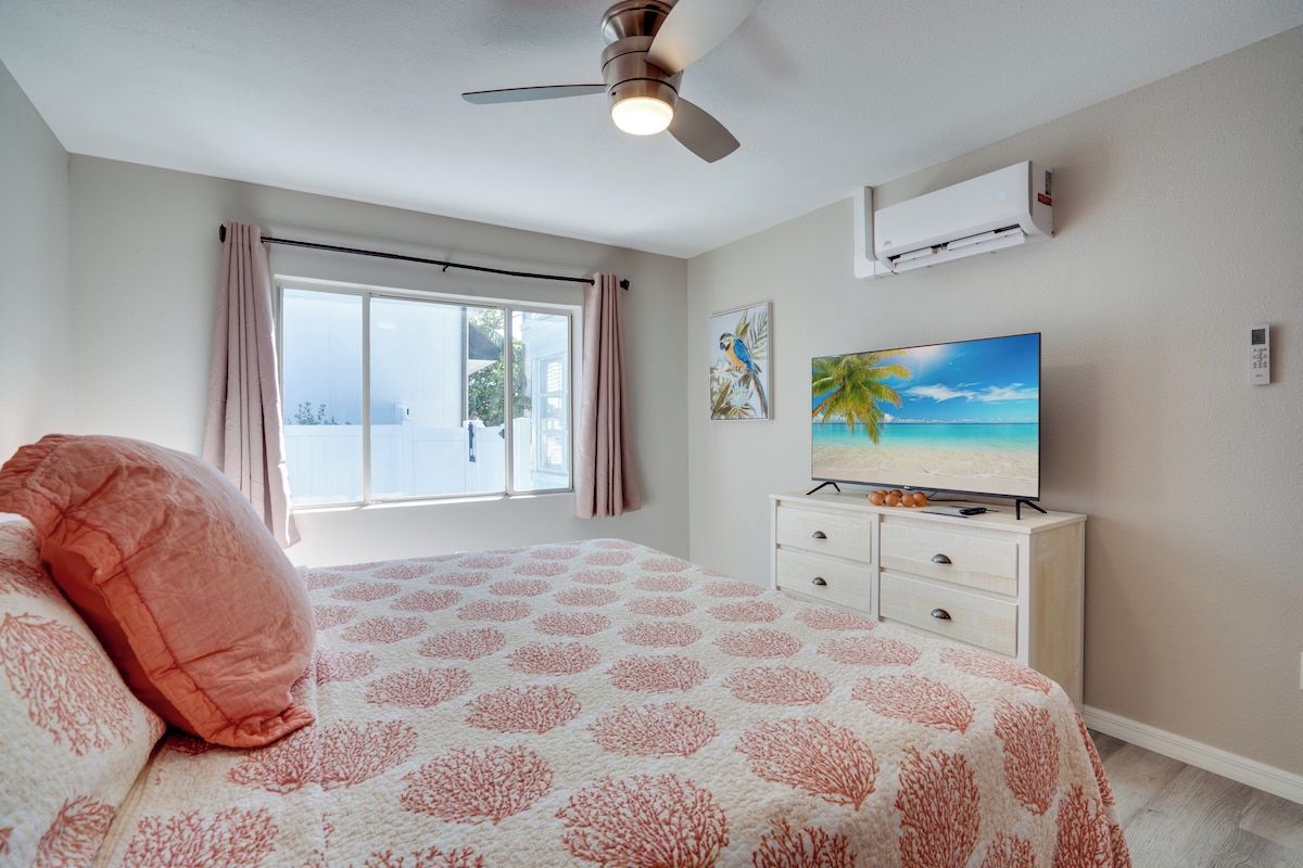 A bedroom with a bed, a ceiling fan, a TV, and a window with curtains.