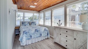 A bedroom with a wooden ceiling, a large bed with a blue floral bedspread, white walls, and a window with blinds. - Across from the beach - Bella by the Sea by SeaBreeze Vacation (Bradenton Beach)
