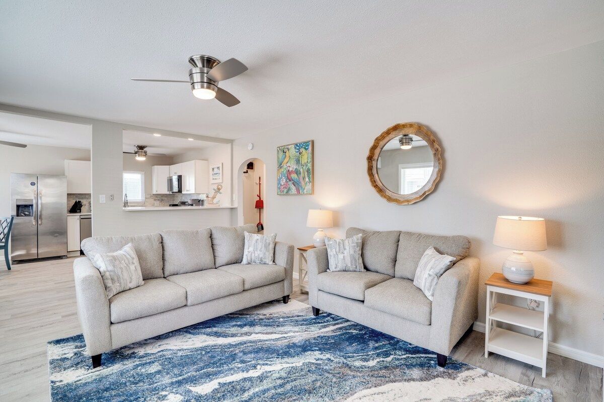 A living room with two sofas, a blue rug, a ceiling fan, and a kitchen in the background.
