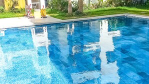 Una piscina rectangular con agua azul cristalina, rodeada de césped y algunas plantas.