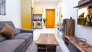 Una sala de estar moderna con un sofá, una mesa de centro, un televisor y una cocina visible al fondo.