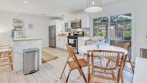 A modern kitchen with white cabinets, stainless steel appliances, and a dining area with wicker chairs and a white table. - Private Cottage Oasis w Pretty Porch + Splash Pool (St Simons Island)