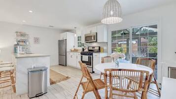 Een moderne keuken met witte kasten, roestvrijstalen apparatuur en een eethoek met rieten stoelen en een witte tafel.