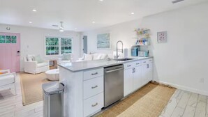 A modern kitchen with white cabinetry, a stainless steel dishwasher, and a large window. - Private Cottage Oasis w Pretty Porch + Splash Pool (St Simons Island)