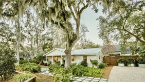 A white house with a metal roof, surrounded by lush greenery and a stone pathway. - Private Cottage Oasis w Pretty Porch + Splash Pool (St Simons Island)
