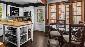 A kitchen with white cabinets, a wooden island, and a dining area with wicker chairs and a glass table. - 
7 BR historical estate near old town (Alexandria)