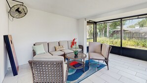 Ein modernes Wohnzimmer mit einer Couch, Sesseln, einem Couchtisch und einem großen Fenster mit Blick ins Grüne.