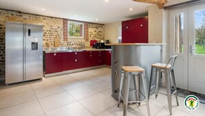 Een moderne keuken met een spatwand van natuursteen, rode keukenkastjes, een roestvrijstalen koelkast en een bar met krukken.