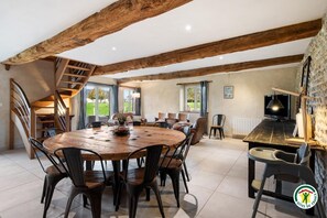 A spacious dining area with a wooden table and chairs, a staircase, and a stone wall. - Gîtes de France® - Gîte L'In et L'Autre (SAINT AUBIN ROUTOT)