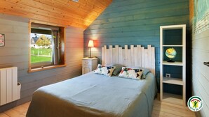 Een knus slaapkamer met een houten plafond, een bed met bloemenkussens, een nachtkastje, een lamp en een wereldbol op een plank.