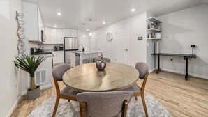 A modern kitchen with white cabinets, a stainless steel refrigerator, and a dining area with a round wooden table and four grey chairs. - Hummingbird Haven-Prime location in South Longmont-sleeps 8,4beds,blocks to Rec (Longmont)